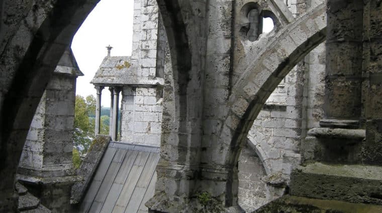 Cathedral roof made of old stone, moss on some areas, two people walking up slanted area, one smiling at camera.